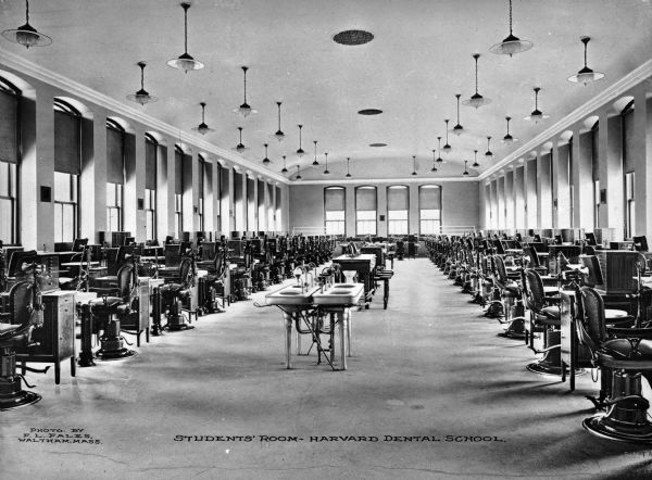 Interior of the students' room at Harvard University Dental School, founded in 1867. The large hall is filled with dental chairs and other equipment. Caption reads: "Students' Room — Harvard Dental School."