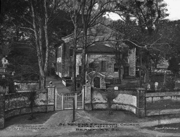 Elevated view of Saint Helena Episcopal Church, established in 1712, and built in 1724. A brick fence and a gate surround the church and cemetery. Caption reads: "St. Helena Episcopal Church, Established 1712. Beaufort, S.C."