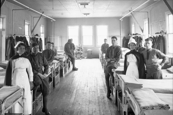 View of Ward 15 of the United States General Hospital No. 7, as designated by the surgeon-general in 1918. Intended for returning soldiers' physical reconstruction, Roland Park's facility specialized in the treatment of the blind and deaf. Two nurses and a group of patients pose in the ward near beds.