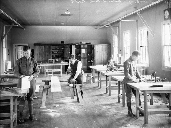 View of blind men learning carpentry skills at the United States General Hospital No. 7, as designated by the surgeon-general in 1918. Intended for returning soldiers' physical reconstruction, Roland Park's facility specialized in the treatment of the blind and deaf. Three men work with tools in the carpentry room.