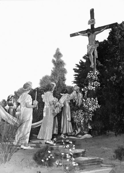 View of a May Crowning ceremony at the Crucifiction Shrine, led by the Sisters of Charity, founded in Pennsylvania in 1870. Women carry a long cloth and candles while walking toward the statue of the crucified Jesus.