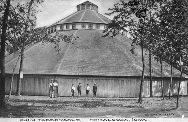 Exterior of a large wooden tabernacle. Four boys and two women stand outside the building. The Caption reads, "C.H.U. Tabernacle."