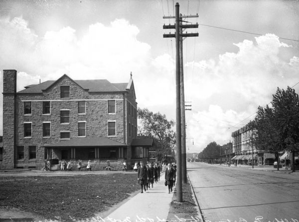 View of Blessed Sacrament Church Rectory. Two rows of children walk on the sidewalk beside telephone poles.