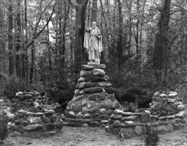 View of a grotto at the Convent of Our Lady of the Cenacle. A statue of a religious man stands atop a base of rocks.