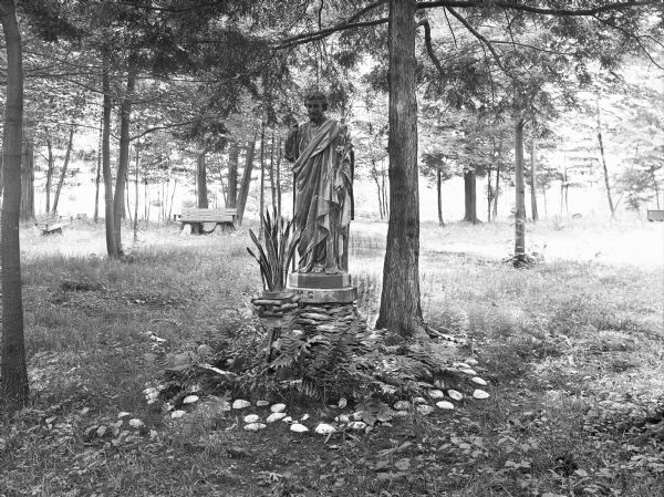 View of a statue of Saint Joseph of the Pines at College Misercordia, established in 1924 by the Sisters of Mercy. Benches can be seen behind the statue, among several trees.