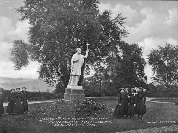 View of a statue of Saint Xavier at Saint Xavier Academy, erected in 1847 by the Sisters of Mercy. Two groups of young women stand on either side of the statue. Caption reads: "'Our Patron Saint' St. Xavier's Academy, Beatty, PA."