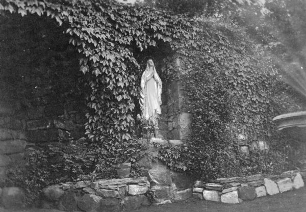 View of the Grotto of Our Lady of Lourdes at Seton Hill College, founded in 1918. A statue of the Madonna stands in a niche in the stone structure covered with vines.