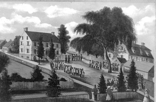 Elevated view of a Moravian funeral on the front lawn of a home. Six men carry a casket toward a group of people playing musical instruments. On either side, groups of people observe the procession.