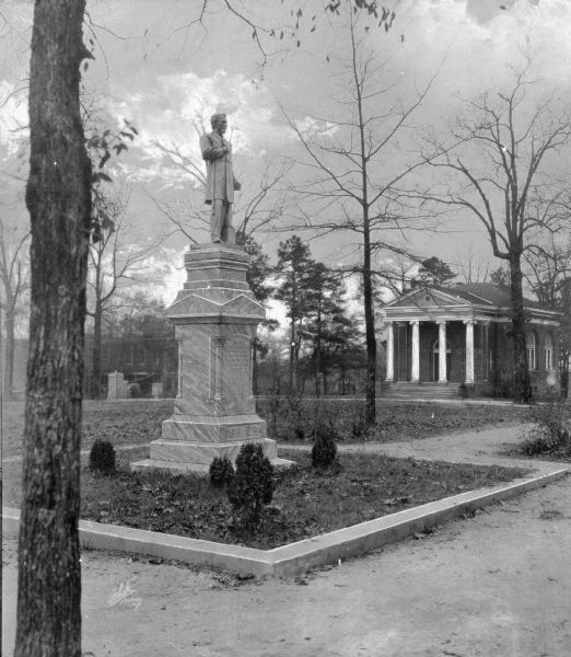 View of a monument to William Moffatt Grier (1843-1899), president of Erskine College from 1871-1899. The monument, erected in 1904, features a statue of Grier standing atop a tablet with text including, "Life's work well done, Life's race well run. Life's crown well won, Now comes rest." In the background is the Euphemian Literary Society Hall, built in 1912, of Erskine College.