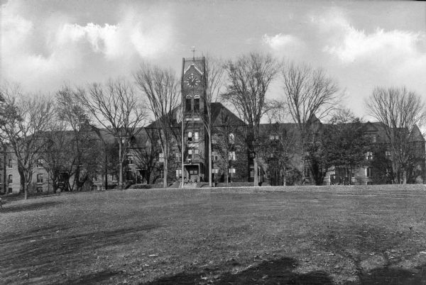 Front view of the exterior of Tilton Hall, built in 1861, part of Tilton School, founded in 1845. Four students sit on the front steps beneath the clock tower.