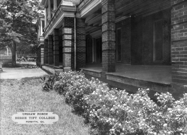 View of the porch of Upshaw Hall built in 1904, at Bessie Tift College.  Flowers line the porch where brick columns support the upper story. Caption reads: "Upshaw Porch, Bessie Tift College, Forsyth, GA."