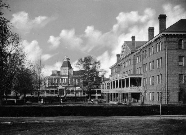 View across campus toward the main buildings of Bessie Tift College, founded in 1849. On the left, Ponder Hall stands, erected in 1883.  Addie Upshaw Hall stands on the right, completed in 1904. Three women stand in the garden between buildings.