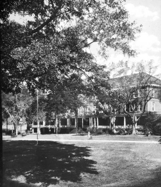 View of Tift Hall at Bessie Tift College, founded in 1849. Trees are on the lawn in front of the hall, and a set of stairs lead to the porch.