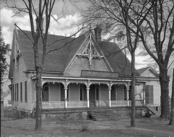 Exterior view of Alsie Imor Chambers Hall at Bessie Tift College, founded in 1849. The Gothic house stands in a wooded area, featuring a set of stairs leading to a porch.