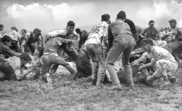 View of a mud fight at Cornell University, which opened in 1868. A group of men struggle in the mud.