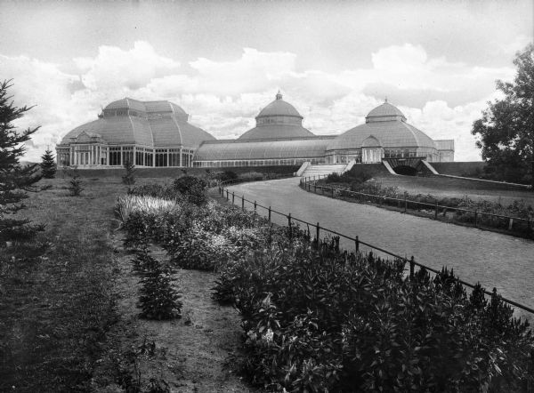Exterior of Enid A. Haupt Conservatory at the New York Botanical Garden, founded in 1896. A path lined by two small fences leads to the door of the building, completed in 1902.