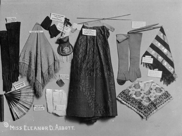 Clothing display containing shoes, a fan, gloves, a shawl, and other items worn by Barbara Fritchie (1766-1862), a heroine who defied General Stonewall Jackson and the invading troops. Labels are attached to most of the items and the clothing, including "Crepe Shawl," "Mits or 'Half'Hands Made & worn by Barbara Fritchie" and "Quilted Silk Petticoat worn by Barbara Fritchie."