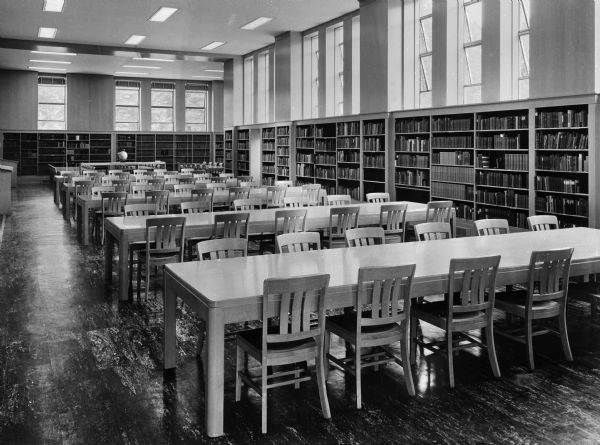 Interior of Brady Memorial Library at College of the Sacred Heart, founded in 1841. Long tables and chairs are surrounded by bookshelves standing against the wall.
