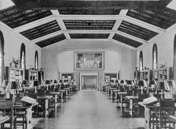 Interior of the reading room at Friedsam Memorial Library of St. Bonaventure University, founded in 1858. The reading room built in 1938 features rows of tables with lamps near bookshelves that line the walls. Above them is a coffered ceiling. A Savonorola painting hangs above the fireplace.