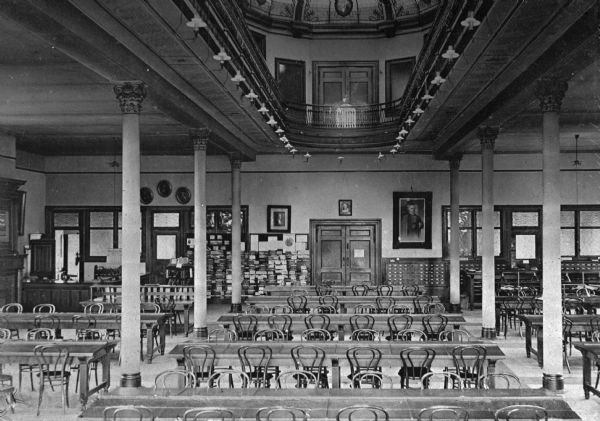 Interior of the library at Slocum Hall, built in 1898. Located on the campus of Ohio Wesleyan University, founded in 1842, the hall features an arcade and a skylight. Rows of tables and chairs are in the room which is separated by columns.