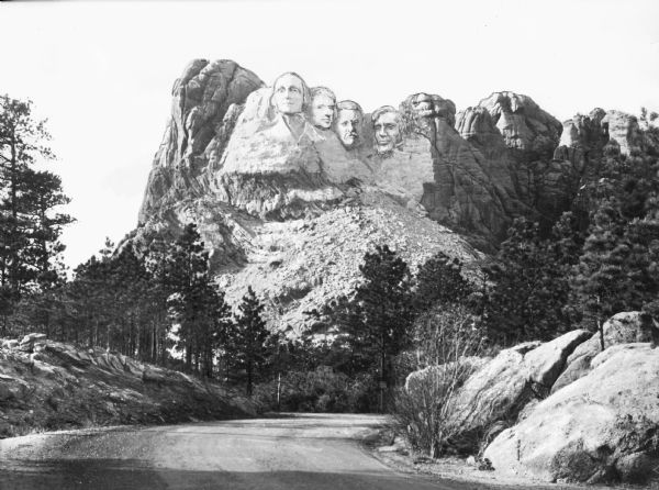 View of Mount Rushmore National Memorial.  A road curves to the right where four presidents are depicted in the granite: George Washington, Thomas Jefferson, Theodore Roosevelt, and Abraham Lincoln.  Construction on the memorial began in 1927 and ended in 1941.