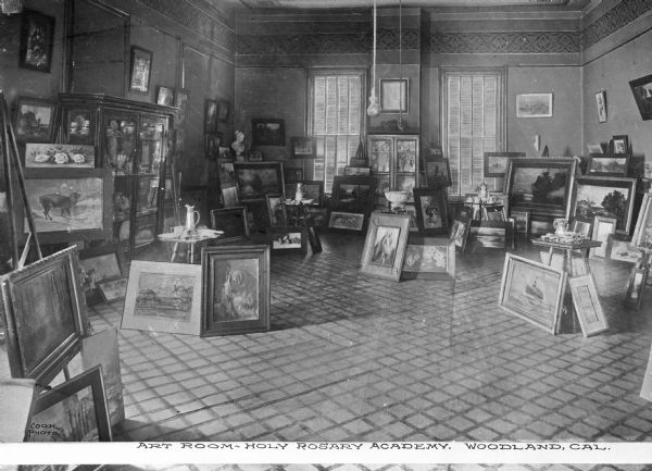 Interior of an art studio at Wilson College, established 1869. The room is filled with sculptures, paintings, tables and easels. Caption reads: "Art Room - Holy Rosary Academy. Woodland, Cal."