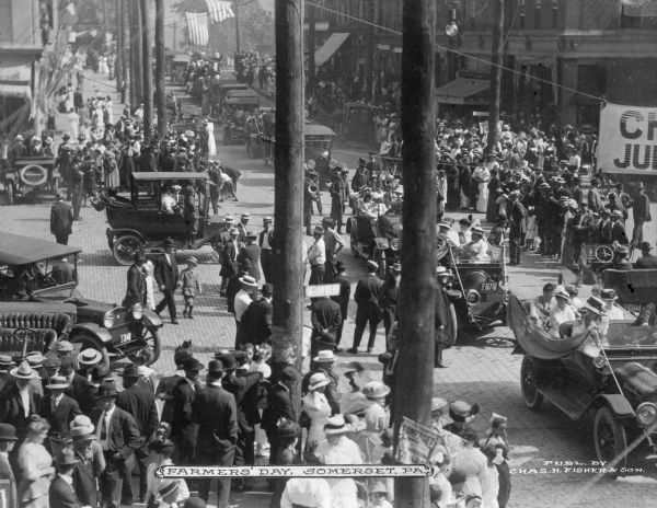 Elevated view of crowds of people and cars in the street on Farmers' Day. Caption reads: "Farmers' Day, Somerset, PA."