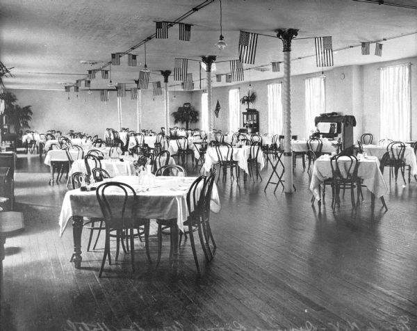 Interior of a dining room at Windsor Hotel, built in the 1880's. The large room is filled with chairs and tables and features a ceiling adorned with flags.
