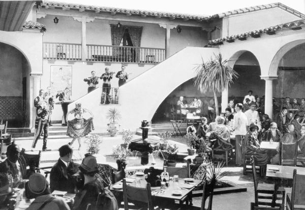 View of a band and dancers at Hotel Agua Caliente, opened in 1928 and dedicated by Wayne McAllister in Tijuana, Mexico. Guests sit at dining tables on the casino patio and observe the show.