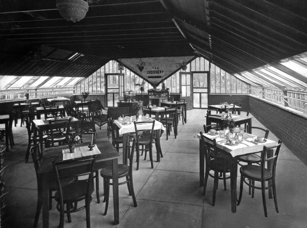 Interior of The Greenery. The restaurant holds tables and chairs, and the dining room is surrounded by windows.