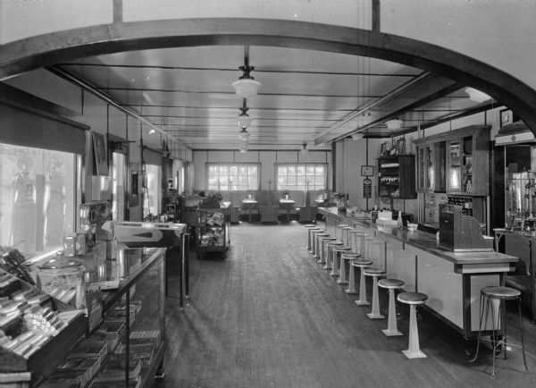 Interior of Molino Service Station and Grill. The building features a counter with stools and a dining space with booths. On the left, there are counters, a pinball machine, and gas pumps are visible through the windows.