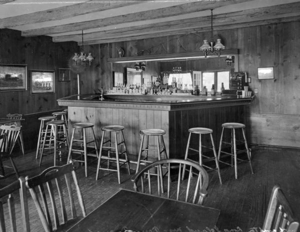 View of a bar and stools inside the Terry Tavern.  A mirror hangs  behind the bar and framed artwork hangs on the adjacent walls.