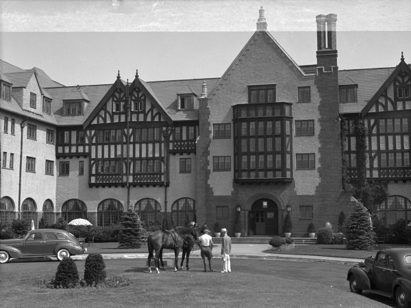 Horses and rider stand on the front lawn of Montauk Manor near a driveway and parked automobiles.  The English Tudor-style hotel opened in 1927.