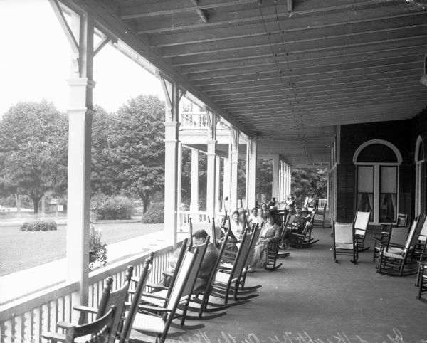 Men and women sit in rocking chairs on the veranda at Poggatticut Lodge.  The lodge was built in 1920.