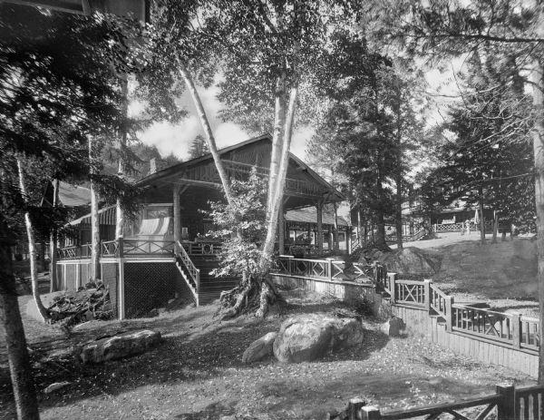 Exterior of a vacation lodge with raised wooden walkways that lead through a wooded area.  The trail to the main lodge continues to the right toward another dwelling in the background.