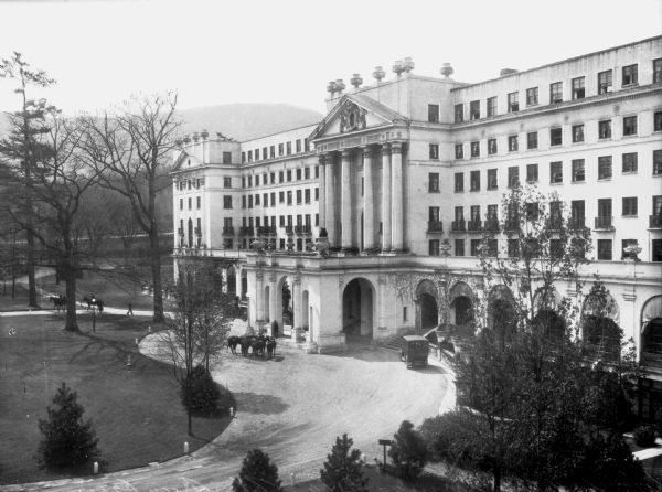 Elevated view toward the driveway and entrance to the Greenbrier Hotel, built in 1913. The building features a port-cochere and a set of stairs leading to the front door. Horses and automobiles are at the entrance.