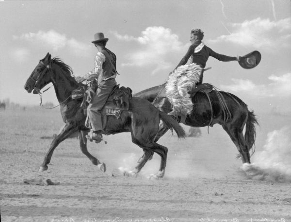 A man is riding a bucking bronco while another man rides in front of him at a "Frontier Days" rodeo.