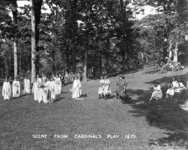 Costumed students act out a scene from Cardinal's Play outdoors on a lawn near a wooded area at the College of Mount Saint Vincent. The college was founded by the Sisters of Charity of New York in 1847. Caption reads: "Scene from Cardinal's Play 1875."
