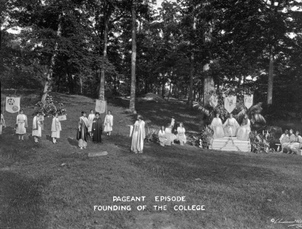 Costumed students stand outdoors to act in a pageant celebrating the founding of the College of Mount Saint Vincent. The school was founded in 1847 by the Sisters of Charity of New York. Caption reads: "Pageant Episode, Founding of the College."