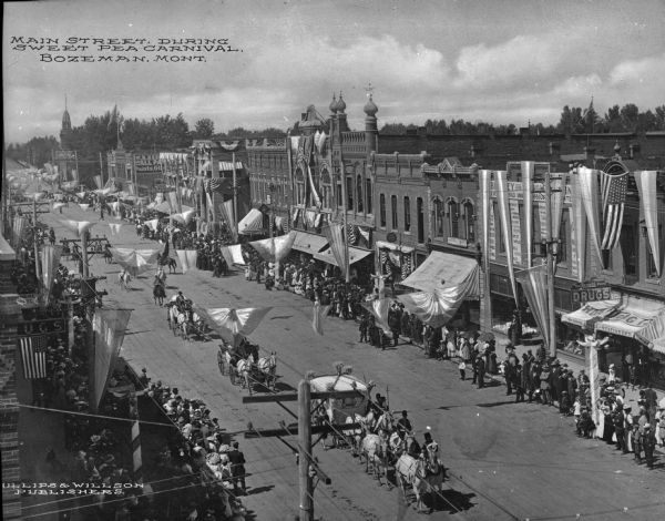 Elevated view of Main Street during the Sweet Pea Carnival. Horse-drawn carriages process down the crowded streets past stores and other buildings. Caption reads: "Main Street During Sweet Pea Carnival, Bozeman, Mont."
