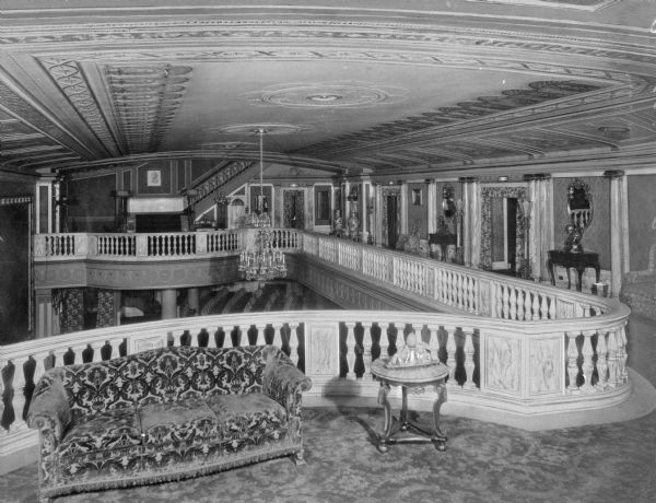 Interior of Loew's Metropolitan Theatre. The mezzanine lounge features a couch, tables, mirrors, and an ornate ceiling overlooking the seating of the ground floor theater. The theater was designed by Thomas Lamb and opened on September 15, 1918.