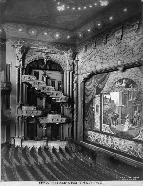 Interior of New Bradford Theatre, built in 1935 in the Hooker Fulton Building. The view taken from the stage left balcony features an ornate stage with a curtain and scenery, the ground floor seating, and the opposite balcony.