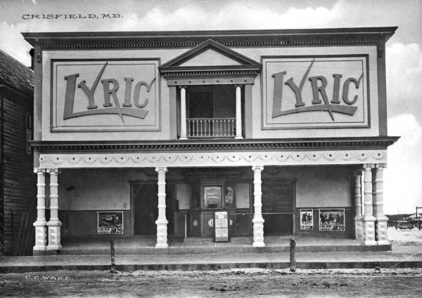 Front view of the Lyric Movie Theatre. An arcaded ground floor features a ticket office and movie posters. Above, a central balcony is flanked by two signs reading. "Lyric."