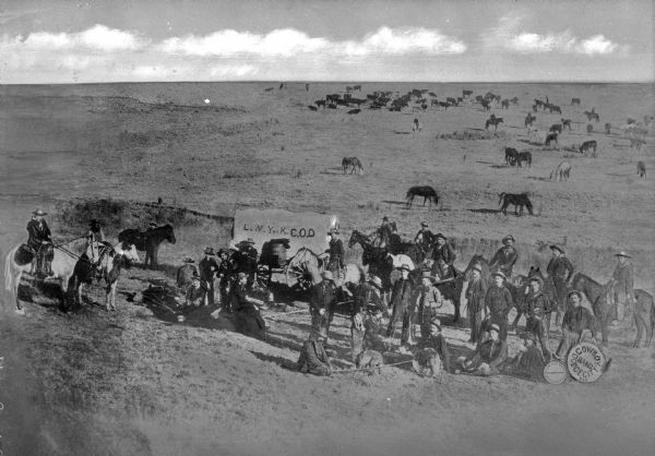 View of a round-up on C.O.D. Ranch. In the foreground, cowboys gather around a chuck wagon labeled, "L.N.Y. or K.C.O.D." The members of the Dodge City Band hold instruments and signs on the right. Beyond the group, more cowboys can be seen on the plain, rounding up and branding cattle.