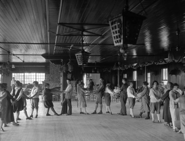 Men and women in a semi-circle holding hands and posing for the camera inside the International Ladies Garment Workers Unity House. The house was rented in 1925.