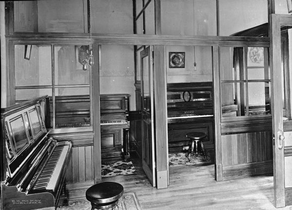 View of practice rooms at Loyola Sacred Heart Academy, established in 1873. Pianos can be seen in individual practice rooms with large windows and wooden doors.