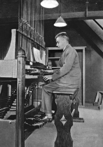A man sits on a wooded bench to play the clavier at Mercersburg Academy, a school organized in 1893. Lighting hangs from the ceiling to illuminate the carillon.