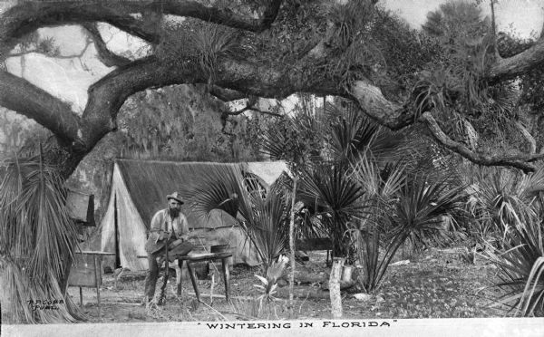 A man holds a gun while standing near a table in a campsite surrounded by palm trees. Caption reads: "Wintering in Florida."