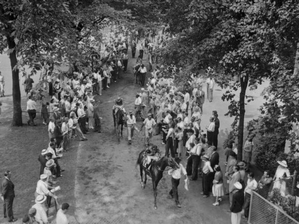 Elevated view of spectators viewing horses as they parade before a race at Saratoga Racetrack. The racetrack opened in 1864.