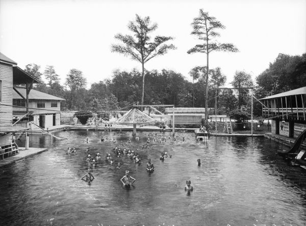 Elevated view of children swimming in a pool between buildings at Segers Bathing Resort. A wooded area surrounds the resort.